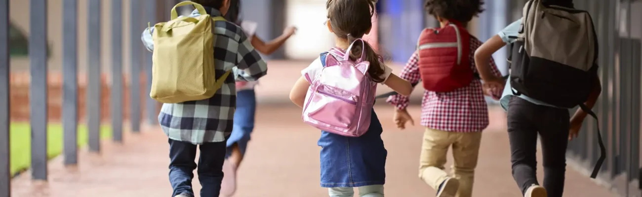 Group Of Multi-Cultural Elementary School Pupils Running Along Walkway Outdoors At School